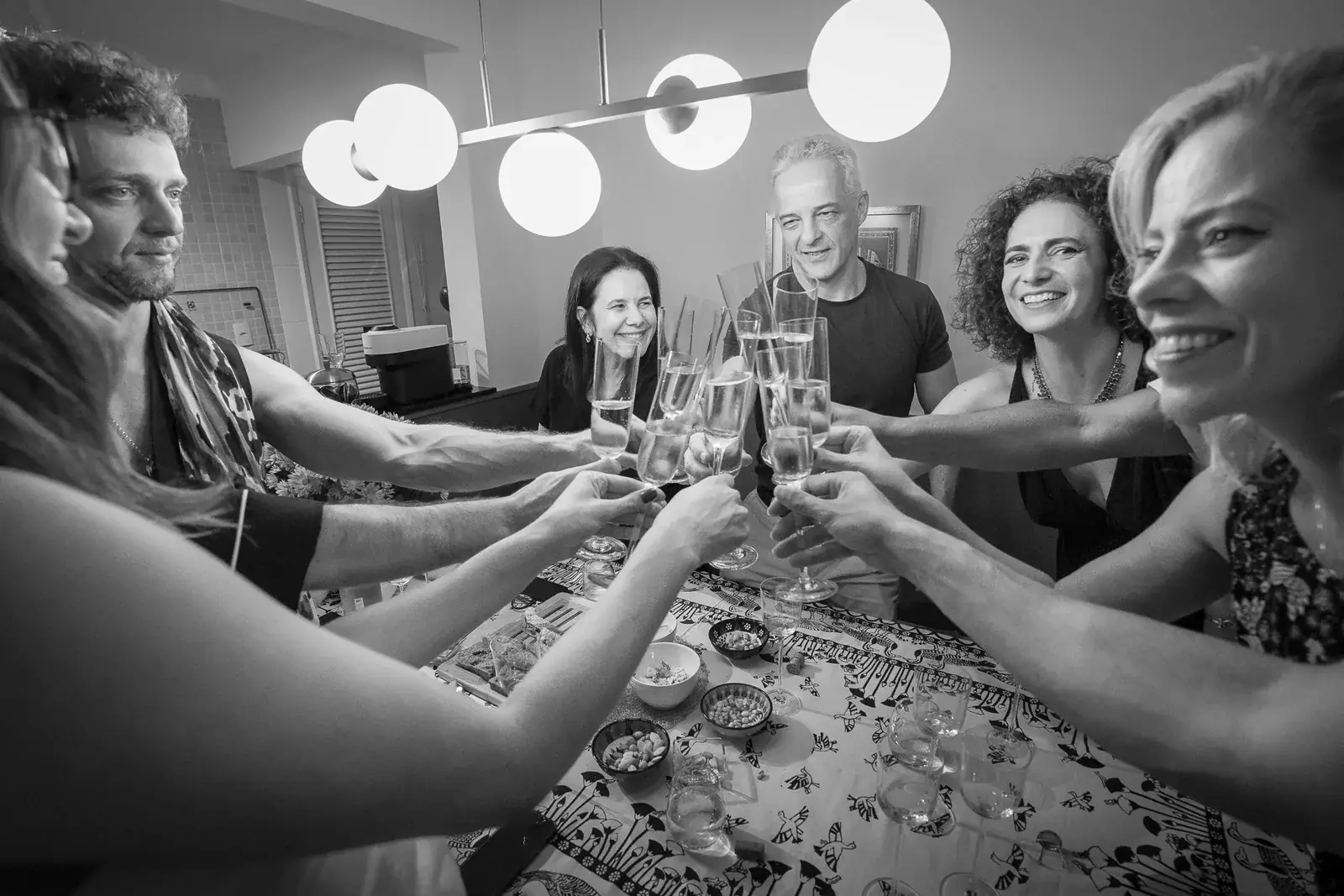Convidados brindando com espumante em volta da mesa, em preto e branco