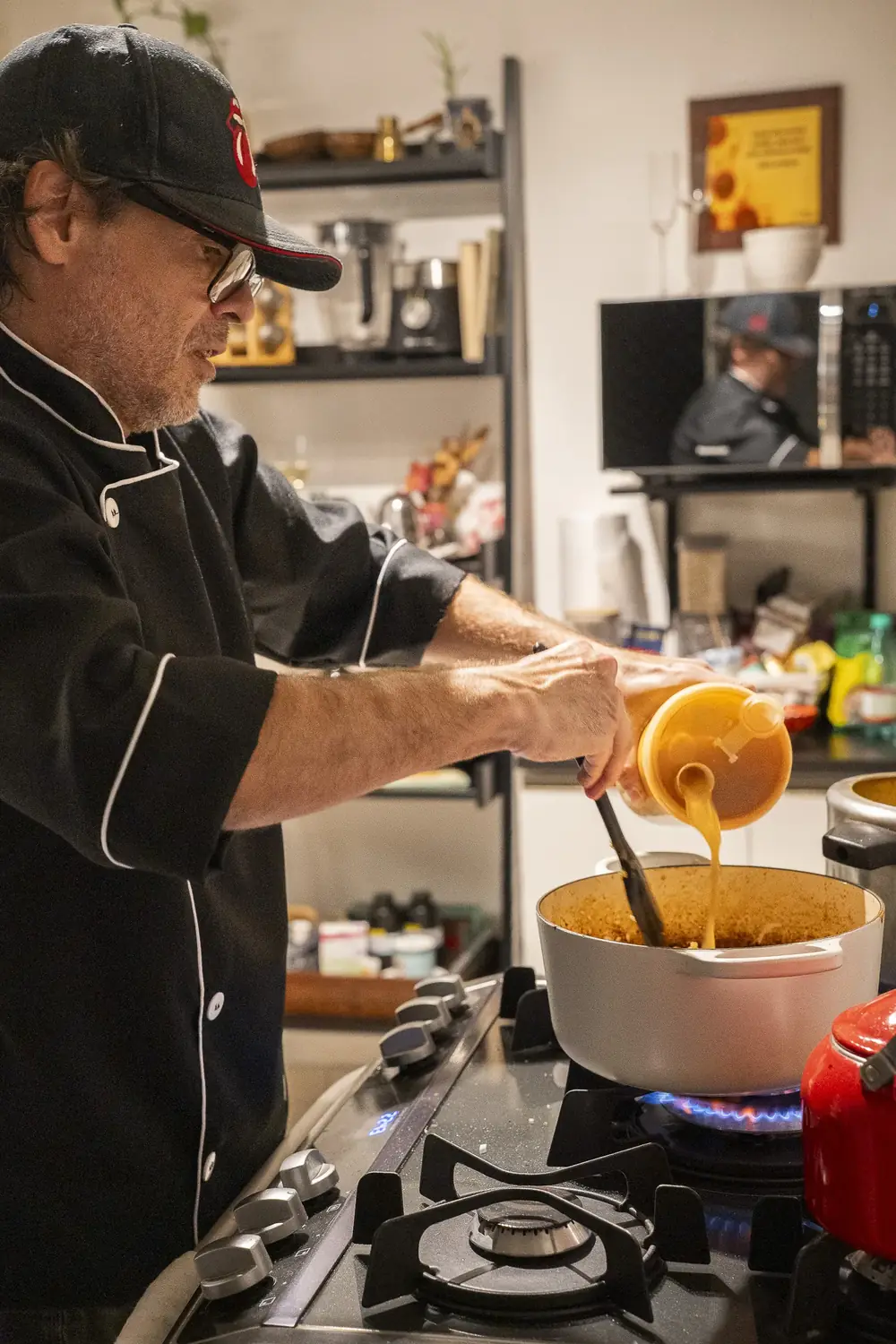 Chef de dólmã e boné servindo com a concha da panela no fogão